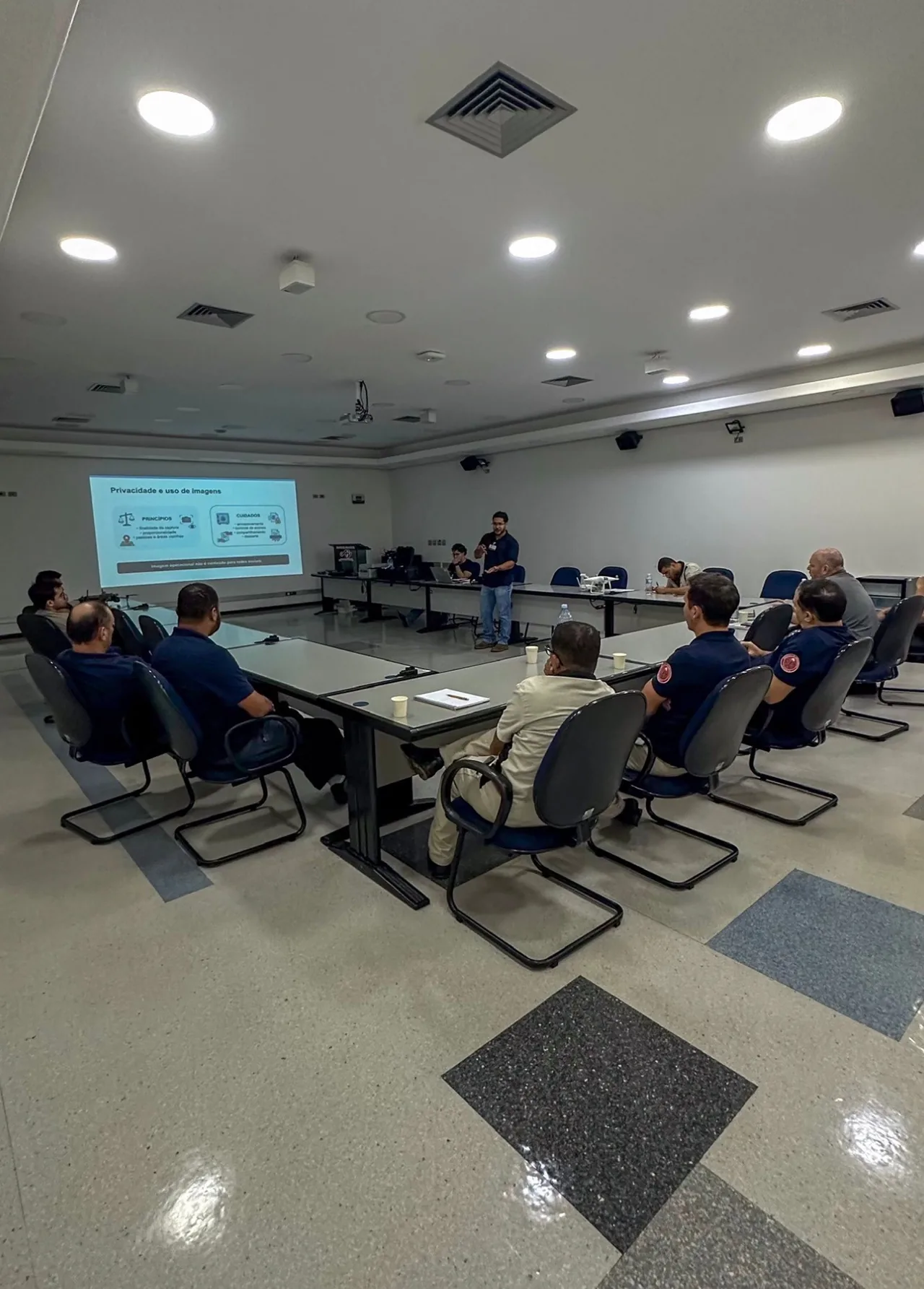 Aula presencial com instrutor, participantes e apresentação projetada.
