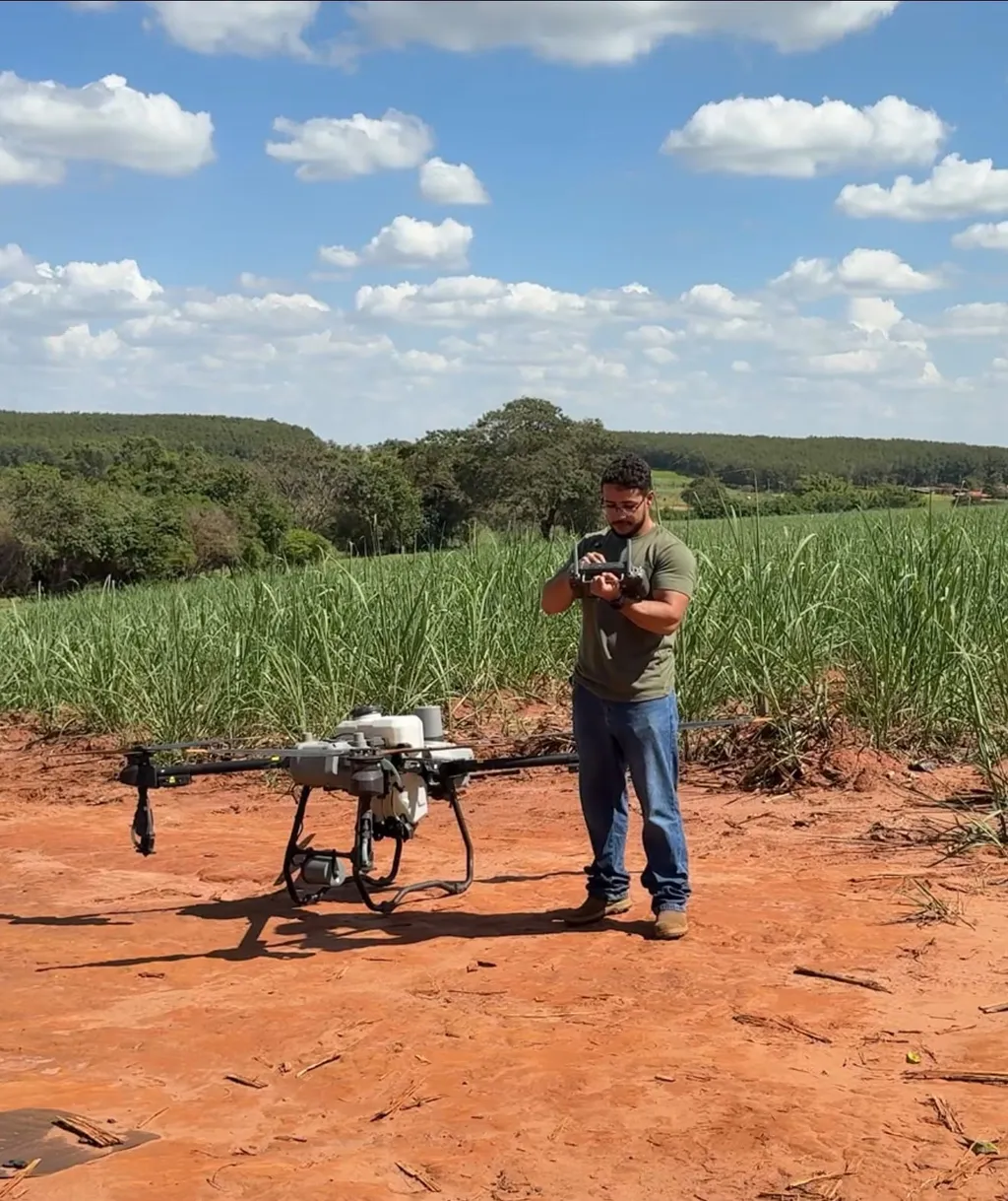 Piloto com controle remoto ao lado de drone agrícola em área de cana-de-açúcar