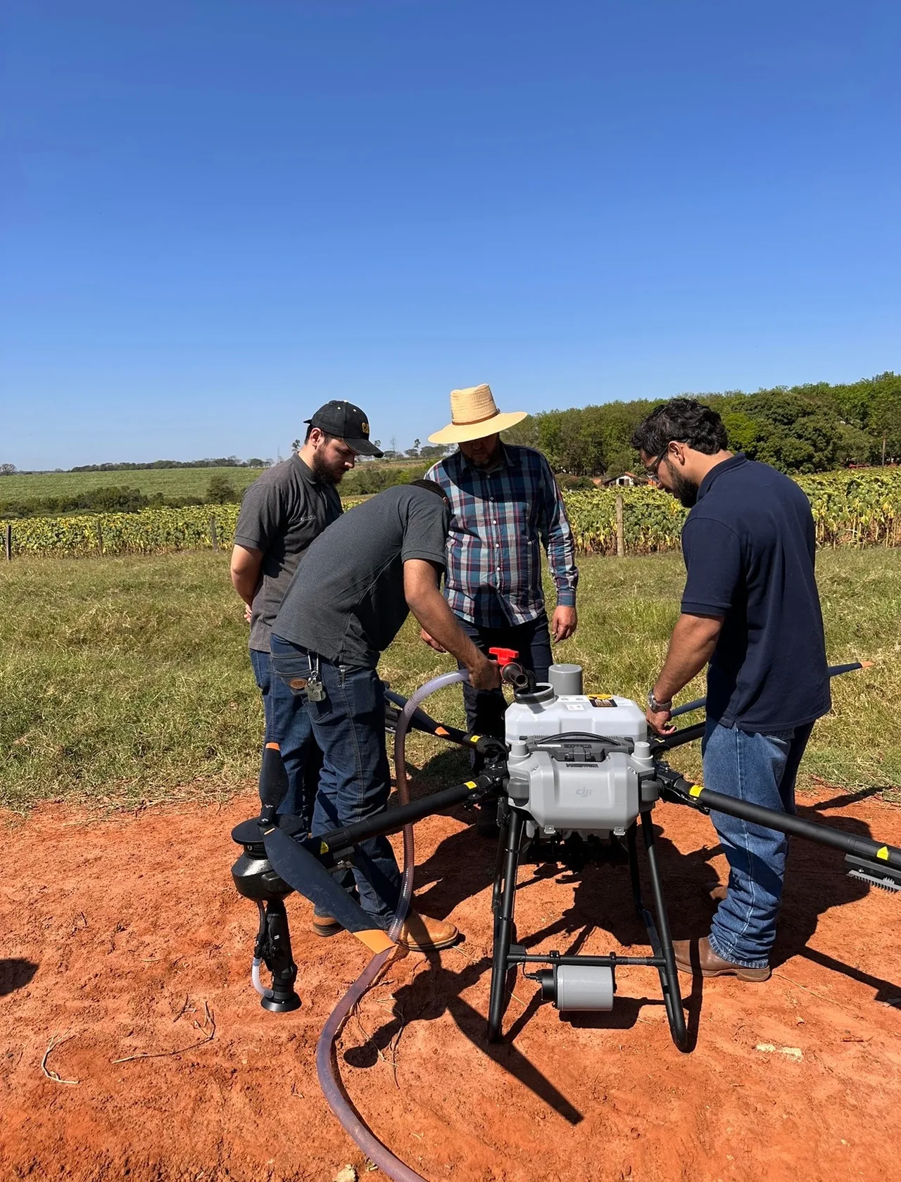 Grupo reunido junto a um drone agrícola em campo.